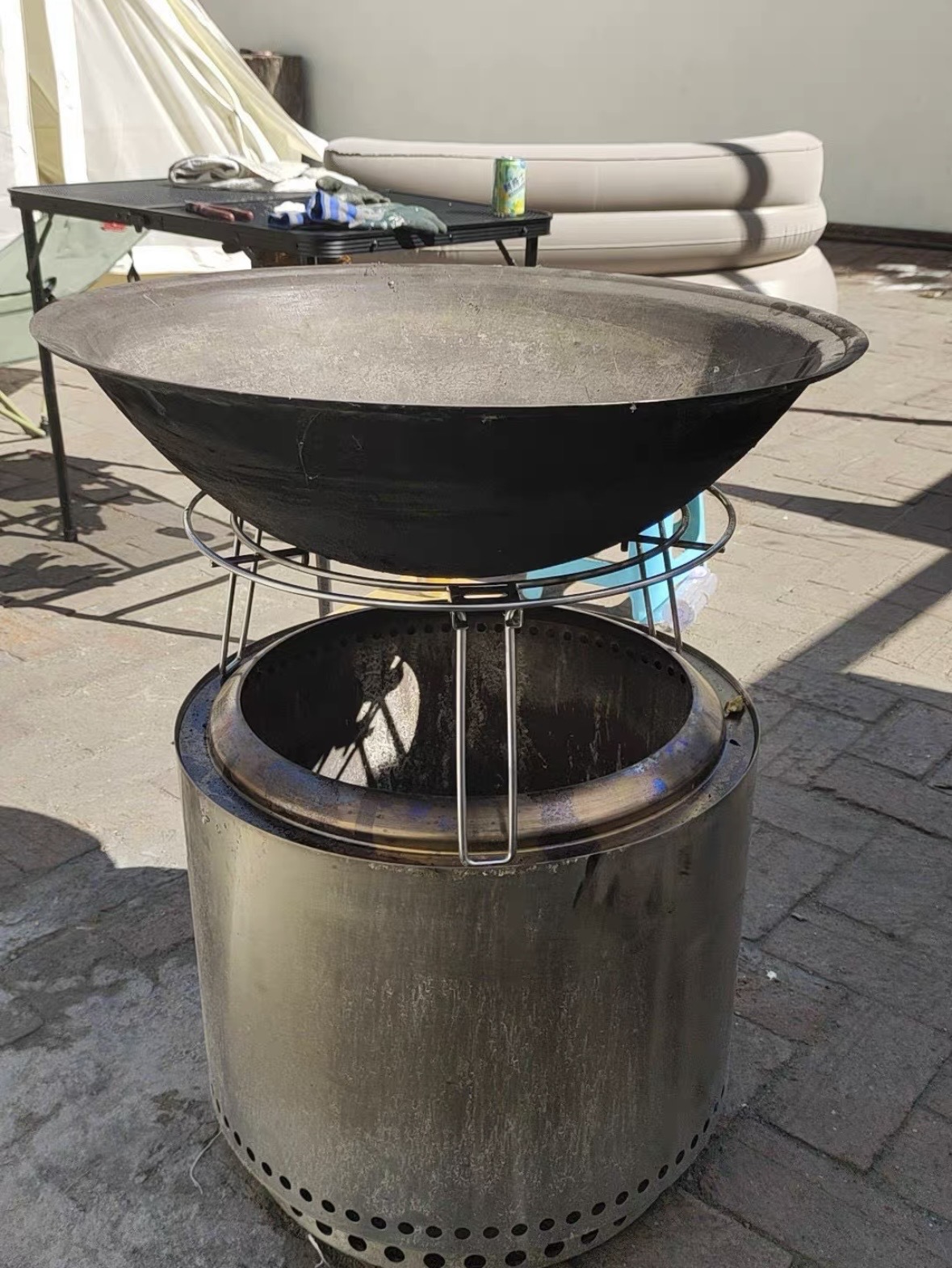 Close-up of a raw stainless steel cylindrical smokeless fire pit showing severe mottled heat tint and surface oxidation colors(blue,purple,straw)after high temperature combustion in an outdoor setting.