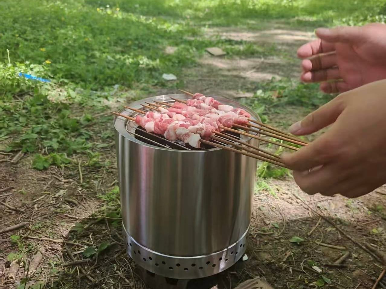 Smokeless fire pit with BBQ grill rack in use outdoors — grilling meat skewers over open flame, camping lifestyle